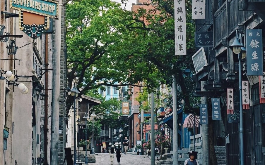 A narrow street lined with traditional buildings, some with signage in a foreign language, and pedestrians walking along. 4
