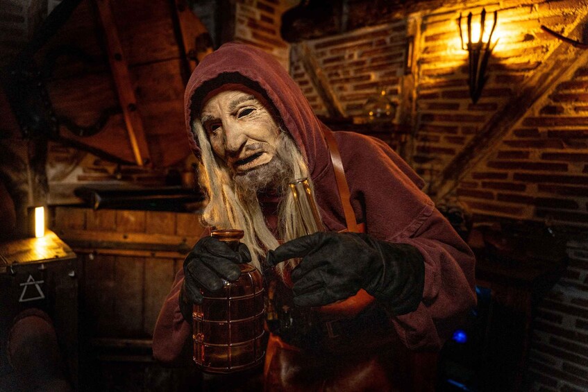 A person in a red hooded cloak holding a glass jar. 1