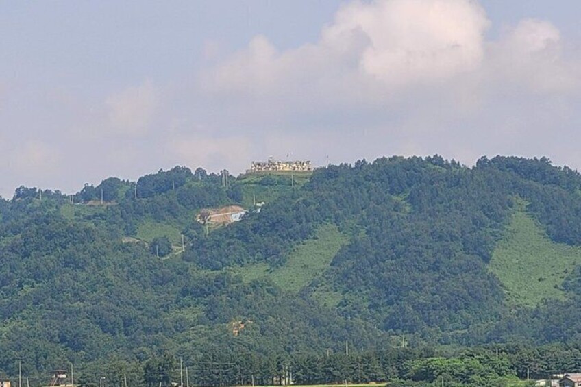 A hill with a building on top, surrounded by dense green forest. 5