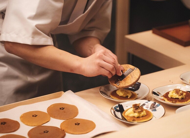 A person slicing a round, flat food item on a wooden board. 2