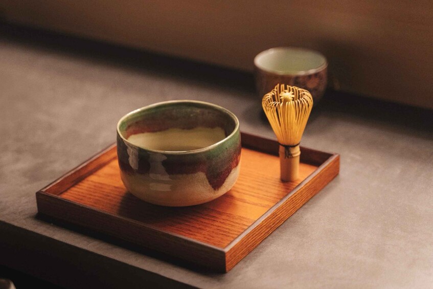 A ceramic bowl and whisk on a wooden tray. 1