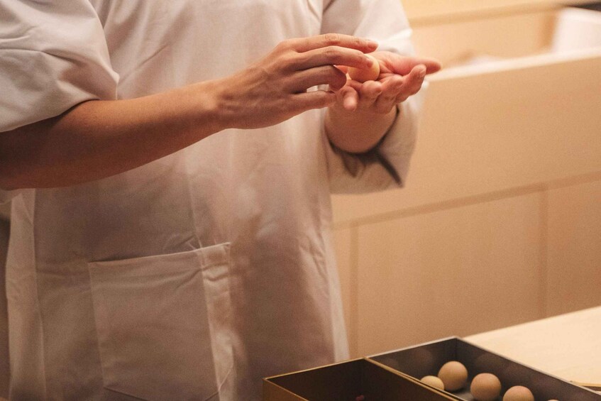 Une personne vêtue d’une chemise blanche et d’un tablier, manipulant des œufs dans une cuisine. 5