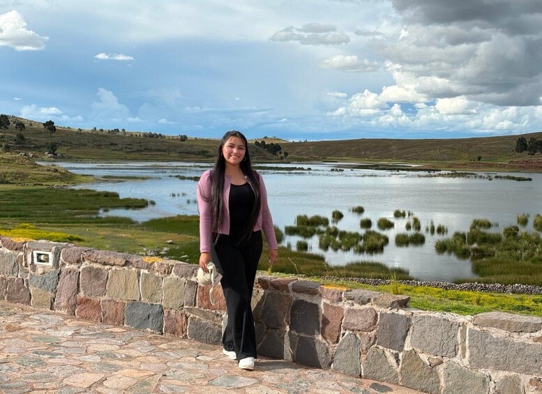 A person standing by a stone wall overlooking a lake with surrounding fields and hills. 3