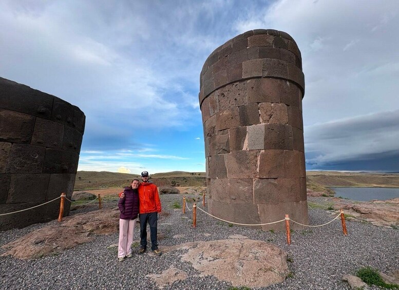 Two people standing in front of a large stone tower with a lake in the background. 5