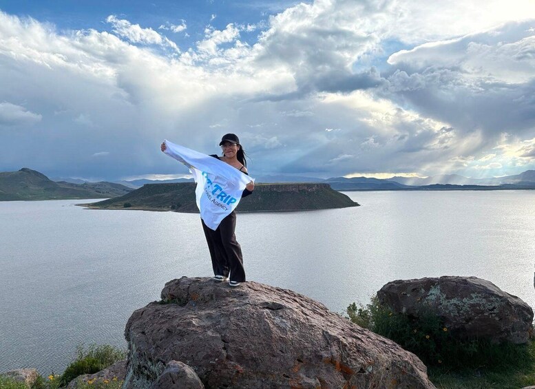 A person standing on a rock by a lake with mountains in the background. 4
