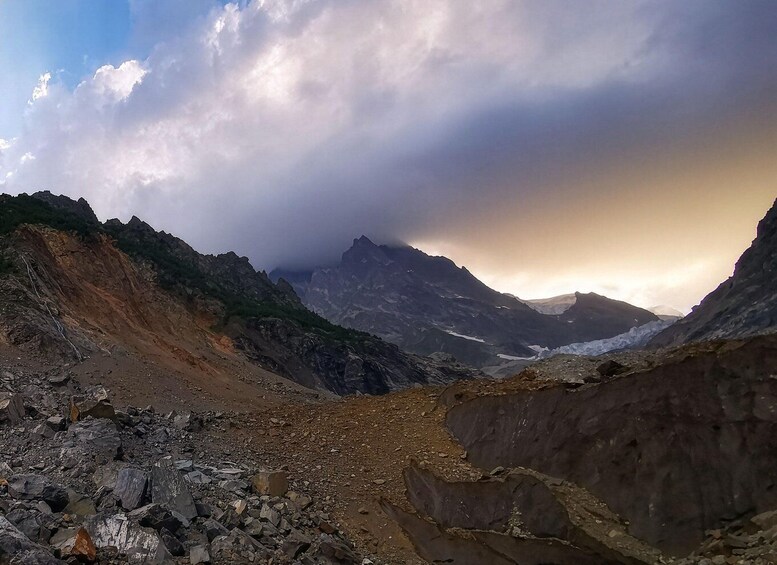 A rugged mountain landscape with a valley, rocky terrain, and a glacier. 1