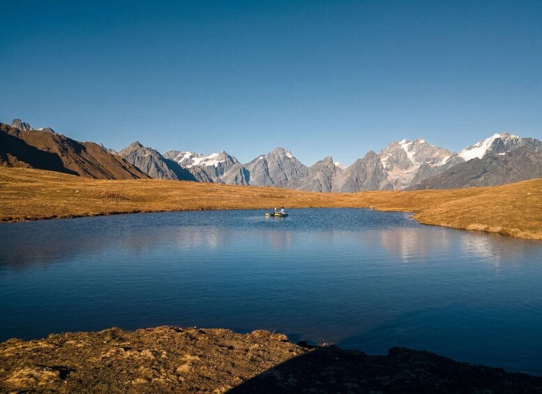 A calm lake with a small boat in the center, surrounded by mountains and a clear sky. 4