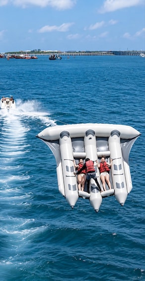 A group of people on an inflatable boat with a wake behind it, in a body of water with other boats and a pier in the background. 2