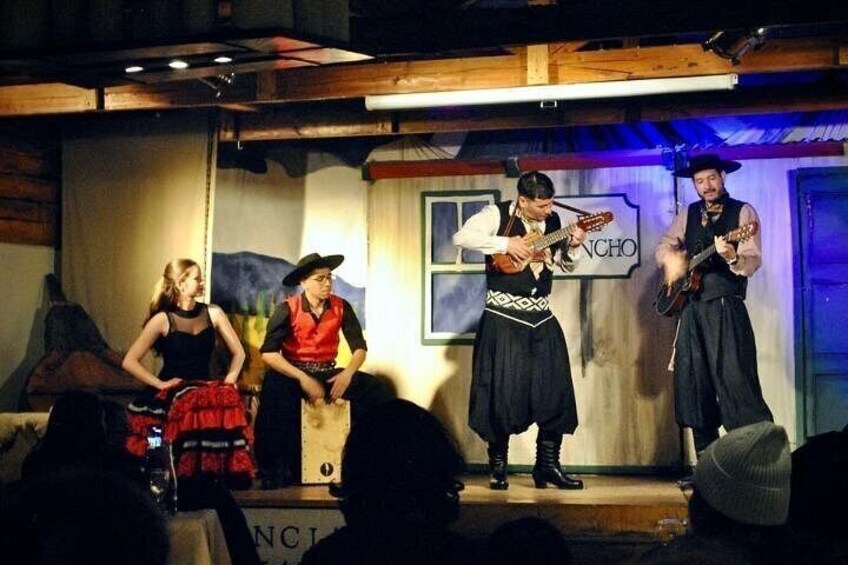 A stage with three performers in traditional attire, a sign reading 'NCHO,' and a wooden backdrop. 3