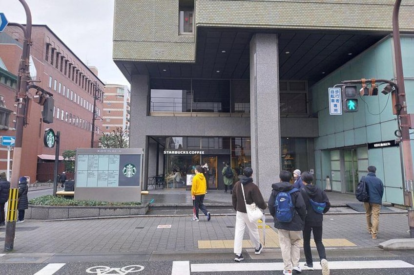 A street with pedestrians crossing, a Starbucks Coffee store, and a building with a green sign. 4