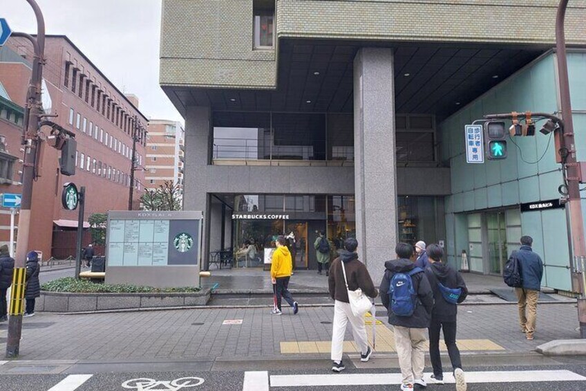 A pedestrian crossing with people walking, a Starbucks Coffee shop, and a modern building with a large column. 2