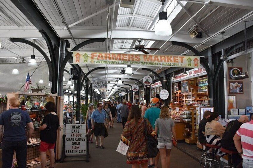 An indoor farmers market with people shopping and vendors selling goods. 1