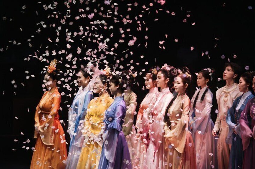 A group of people in traditional costumes on a stage with falling petals. 1