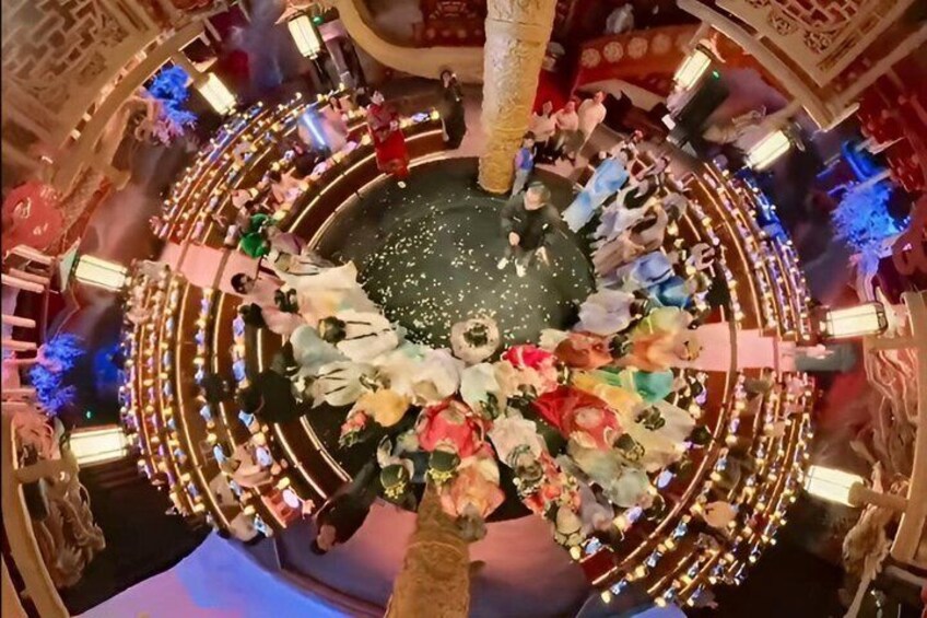 A circular room with a central fountain, surrounded by people and illuminated by decorative lights. 4