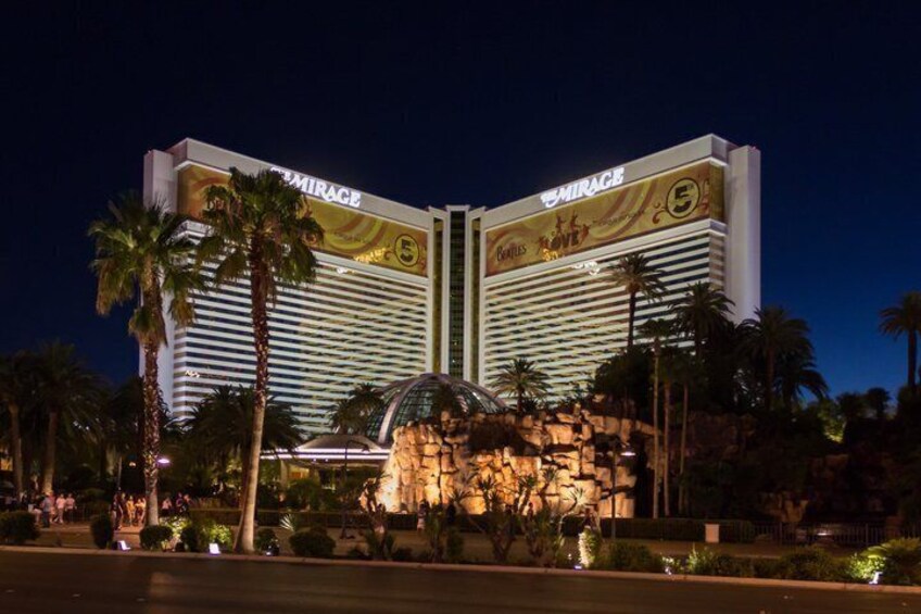 A large, illuminated building with 'Mirage' signage, palm trees, and a rock formation in front. 4