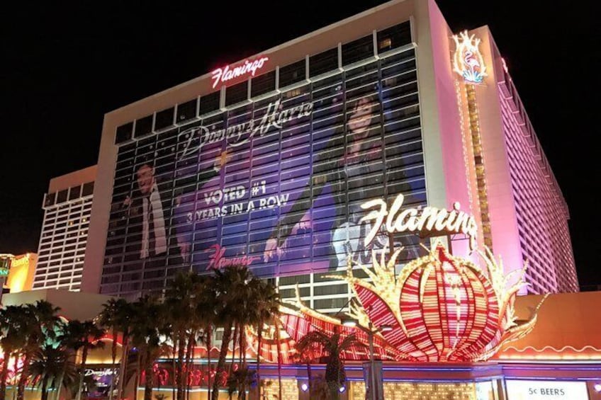 A brightly lit Flamingo Hotel with a large 'Flamingo' sign and a '3 years in a row' award on the facade. 1