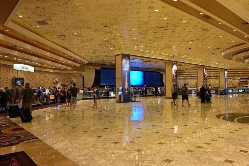 A spacious lobby with marble flooring, a reception desk, and a large screen displaying information. 1