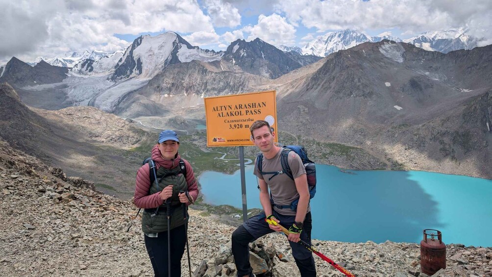 Two hikers on a mountain trail with a sign indicating the Altun Arashan Alakul Pass at 3,920 meters. 1