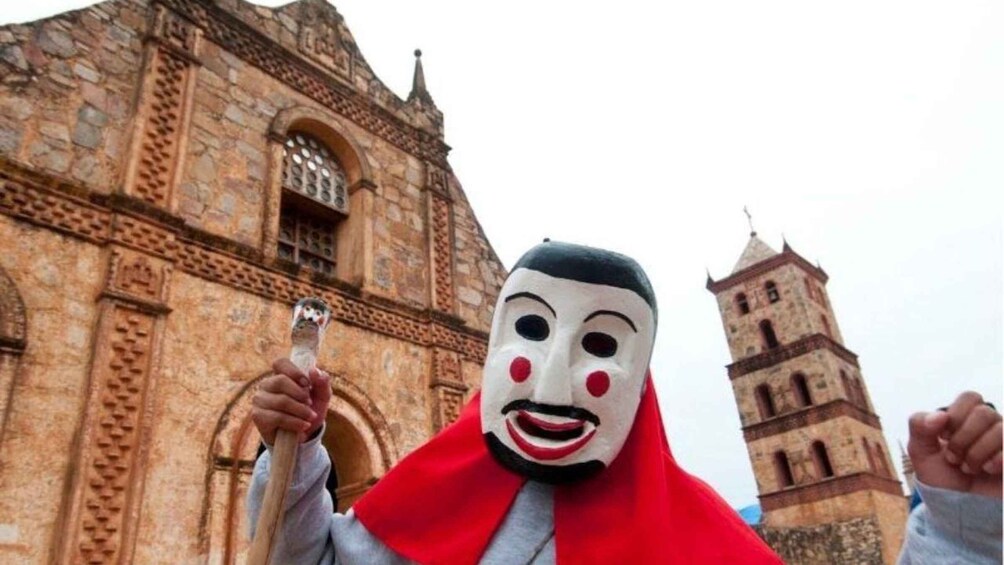 A person in a red cloak holding a book in front of a historic building with a bell tower. 2