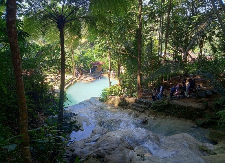 A natural pool surrounded by dense forest, with a small structure and people near the edge. 4