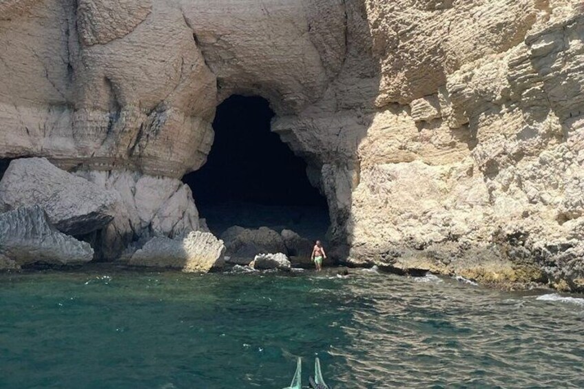 A rocky cave entrance with clear water and a person standing at the edge. 3