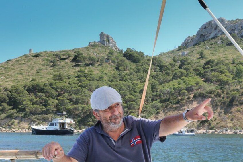 A person on a boat pointing towards a rocky hill with a boat in the background. 1