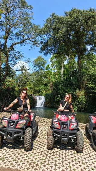 Two people on ATVs in a forested area with a waterfall. 2