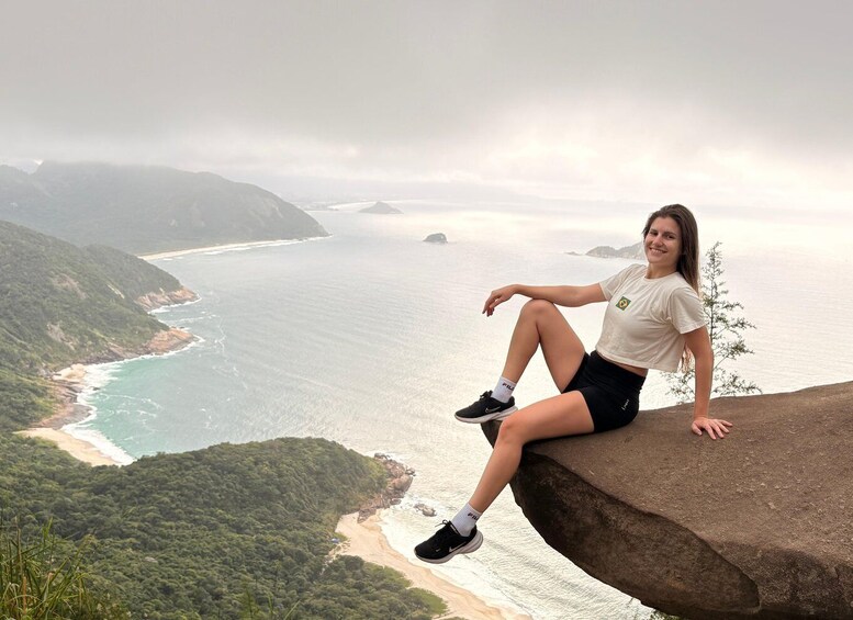 A person sitting on a cliff overlooking a coastal landscape with a beach and ocean. 4
