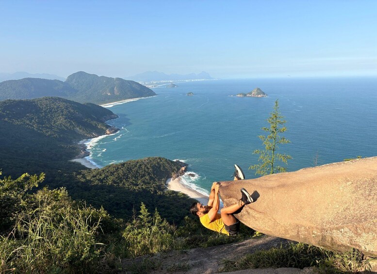 A person sitting on a large rock by a coastal cliff overlooking the ocean. 2