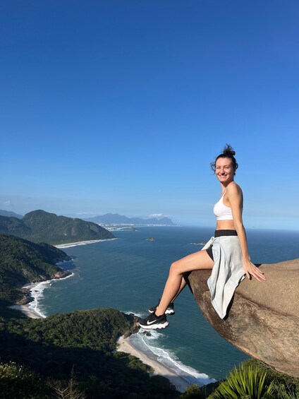 A person sitting on a cliff overlooking a coastal landscape with mountains and the ocean. 3