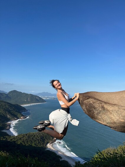 A person climbing a large rock by the ocean with a scenic coastal landscape in the background. 1