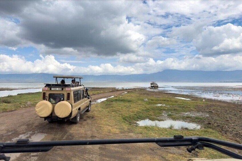 A safari vehicle on a muddy path with a body of water and mountains in the background. 3