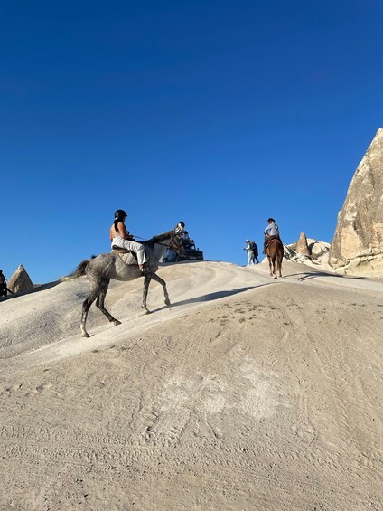 A person riding a horse on a dirt path with rocky formations in the background. 3