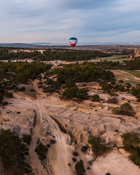 A hot air balloon over a rugged landscape with sparse vegetation and a dirt road. 2