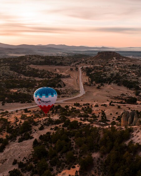 A hot air balloon over a desert landscape with a winding road and distant mountains. 5