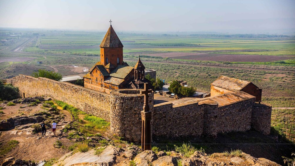 A historic stone church with a bell tower, surrounded by a stone wall and set against a rural landscape. 4