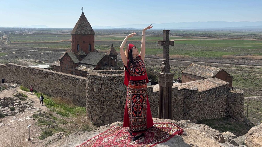 A person in traditional attire standing on a stone wall with a rural landscape in the background. 2