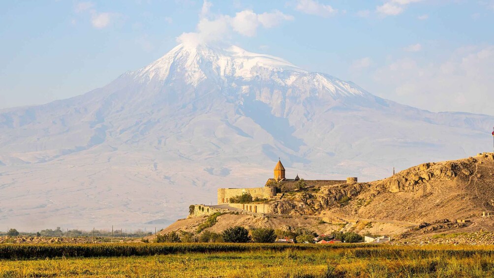 A snow-capped mountain, a historic building with a dome, and a field in the foreground. 1