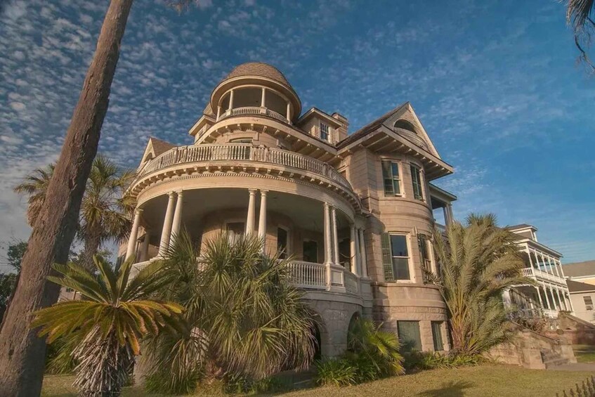 A large, historic mansion with a round tower, columns, and a balcony. 2