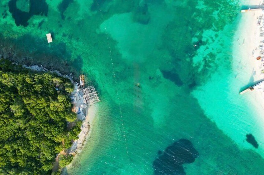 An aerial view of a coastal area with clear turquoise waters, a sandy beach, and a small structure near the shore. 3
