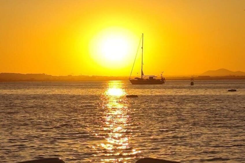 A sunset over a calm sea with a sailboat and distant land. 3