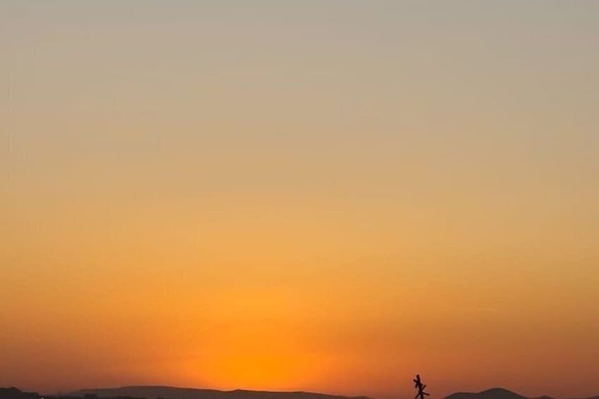 A sunset with a silhouette of a person walking on a flat landscape. 4