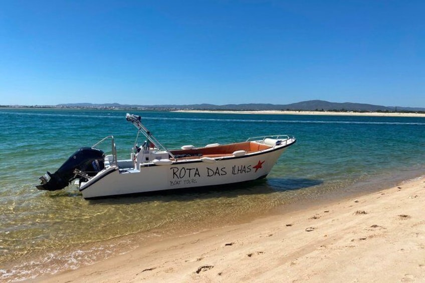 A boat named 'ROTA DAS ILHAS' on a sandy beach with clear water and distant hills. 5