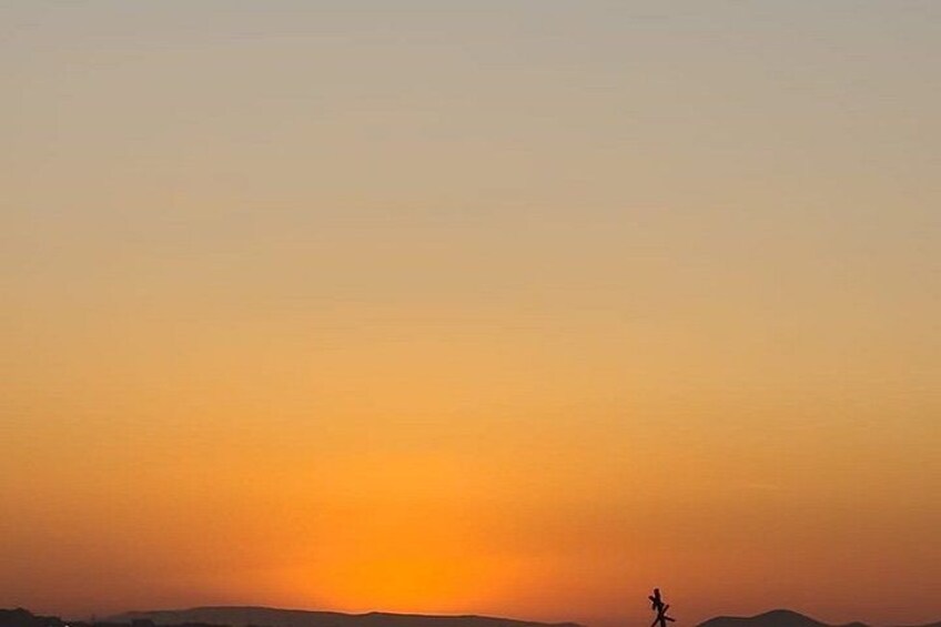 A sunset with a silhouette of a person walking on a flat landscape. 4