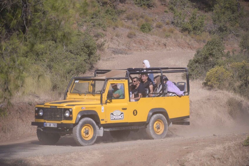 A yellow off-road vehicle with passengers, driving on a dirt road surrounded by dry vegetation. 1