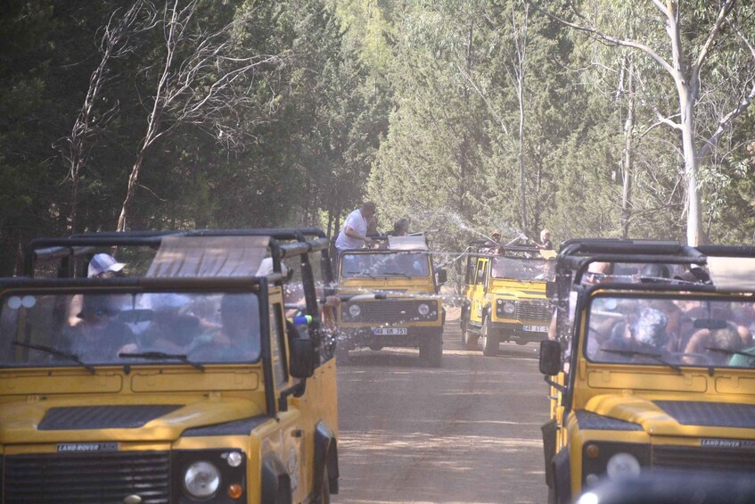 A convoy of yellow Land Rovers driving through a forested area. 5