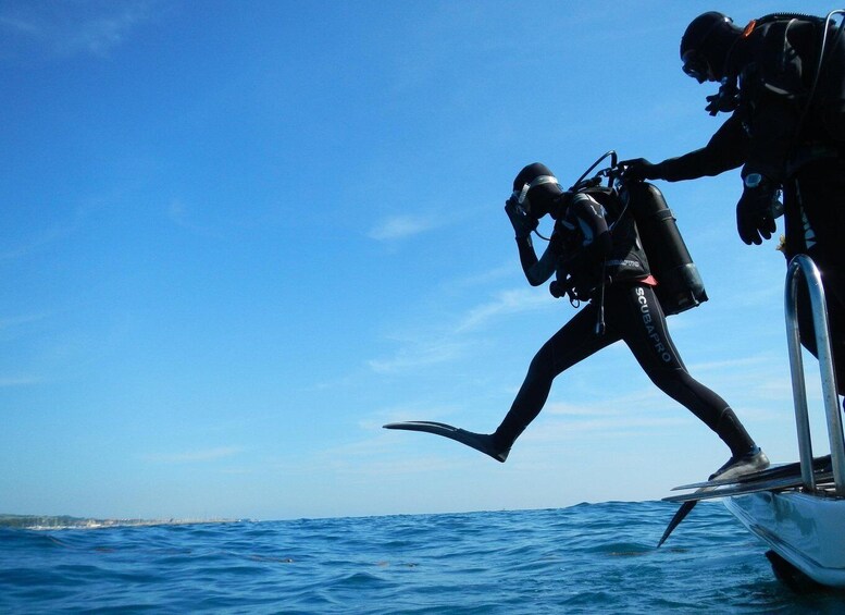 Two scuba divers in black wetsuits and fins on a boat, preparing to enter the water. 1