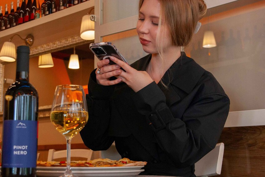 A person seated at a table with a bottle of Pinot Nero wine, a glass of wine, and a plate of food. 1