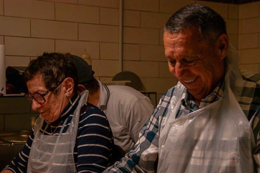 Two people in a kitchen, one wearing a striped shirt and apron, the other in a plaid shirt and apron. 3