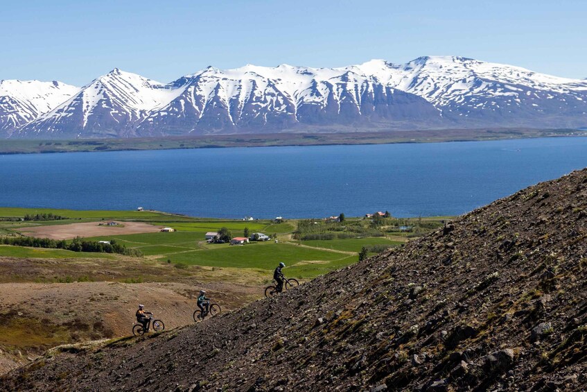 Three mountain bikers on a rocky trail with a lake and snow-capped mountains in the background. 2